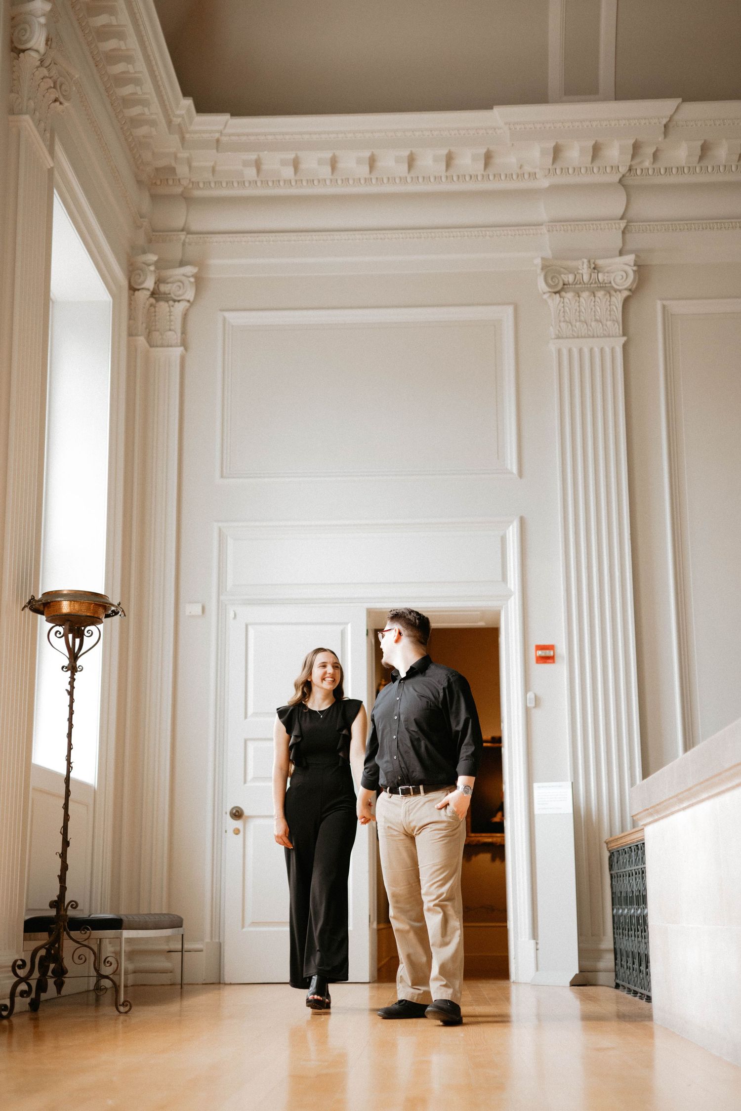 People walking through an elegant white interior space with ornate classical columns and architectural details.