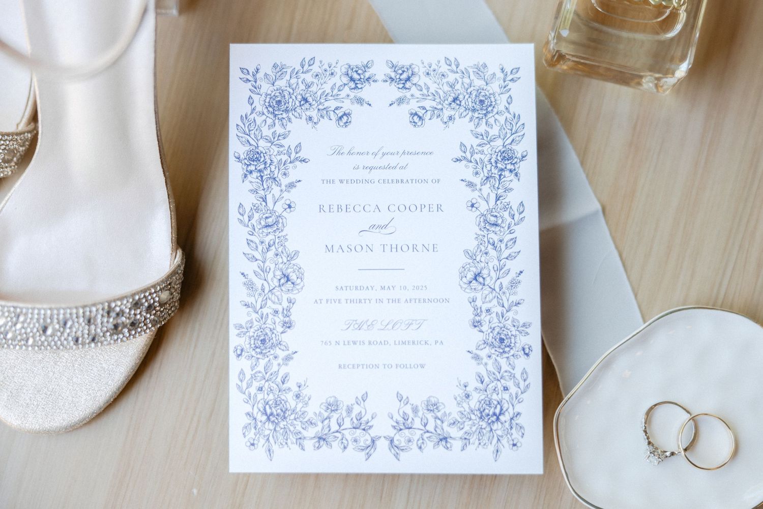 Wedding invitations, rings, and delicate details arranged on a light wooden surface.
