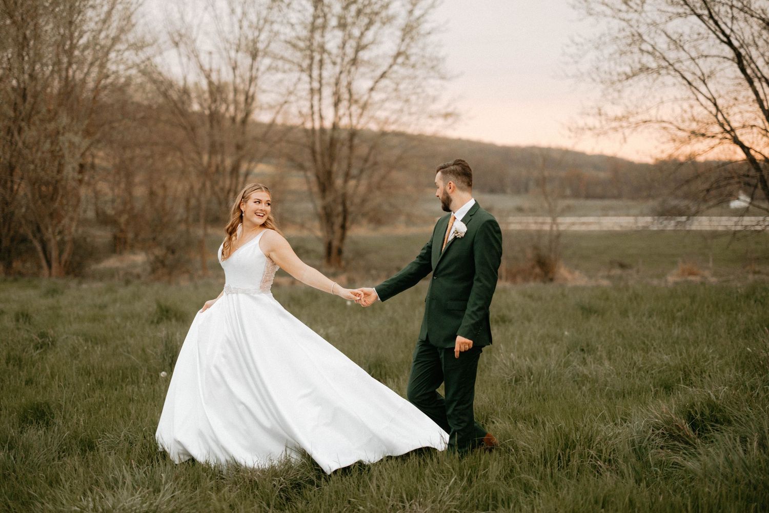 A romantic wedding couple walks through a rustic field at sunset in a cinematic photography series.