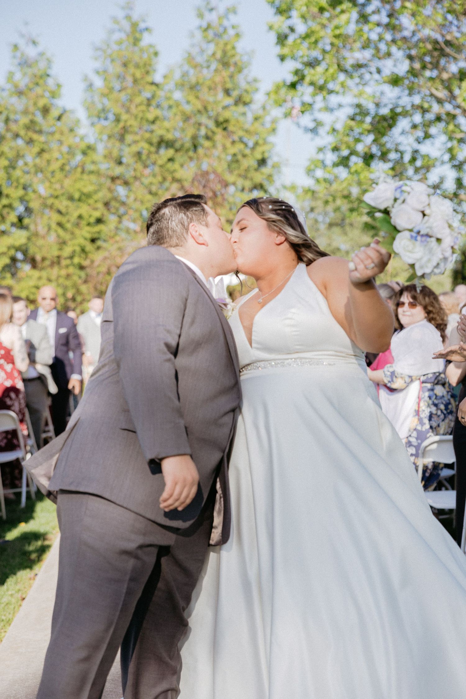 Wedding celebration scene with guests gathered outdoors under blue skies.
