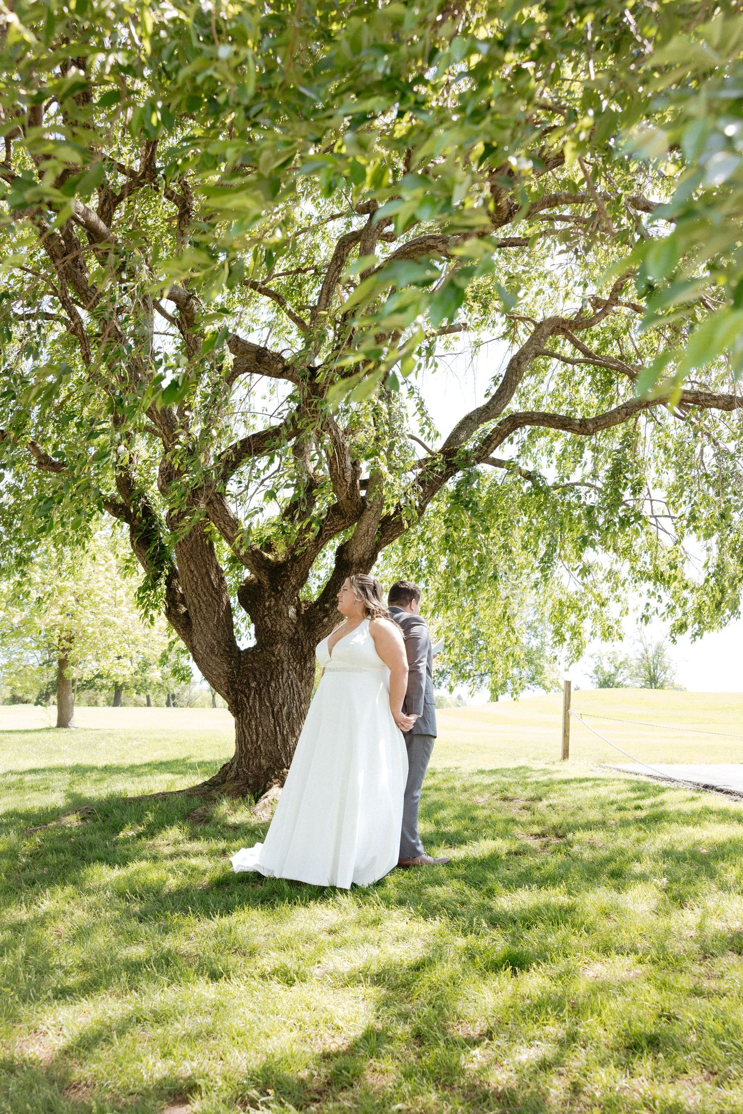 A couple stands beneath blooming apple trees in an orchard on a sunny spring day.