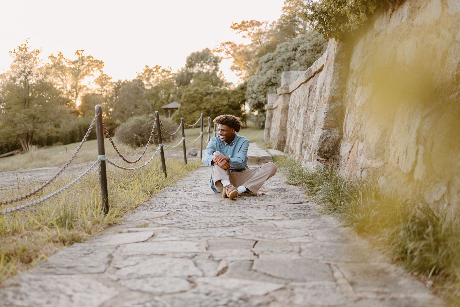 A person sits on stone steps surrounded by ancient ruins during golden hour lighting.