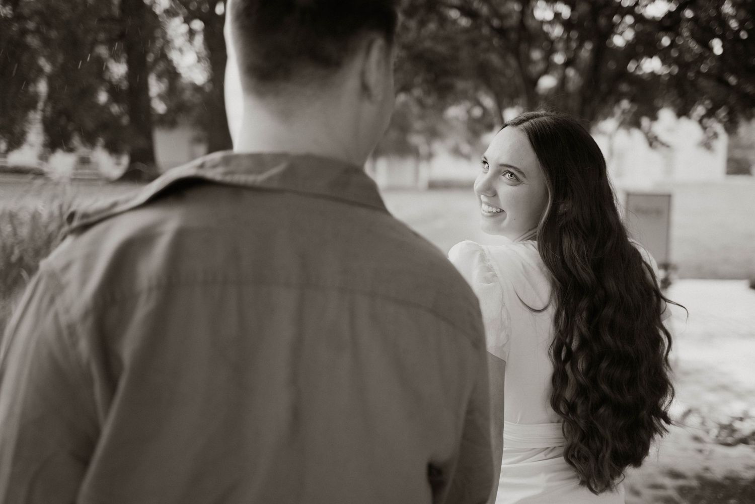 Black and white photo of a couple in a romantic moment outdoors with long flowing dark hair visible.