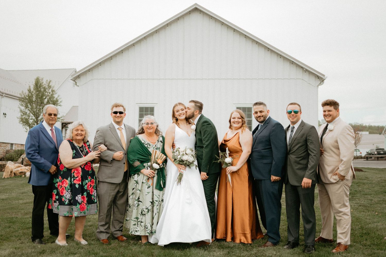 Wedding party poses in front of a white farmhouse building with vibrant fall bridesmaids dresses.