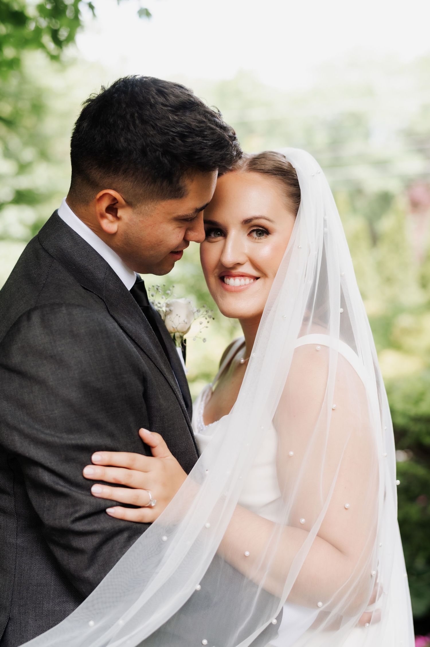 A romantic wedding photo series showing tender moments between newlyweds under a flowing white veil outdoors.