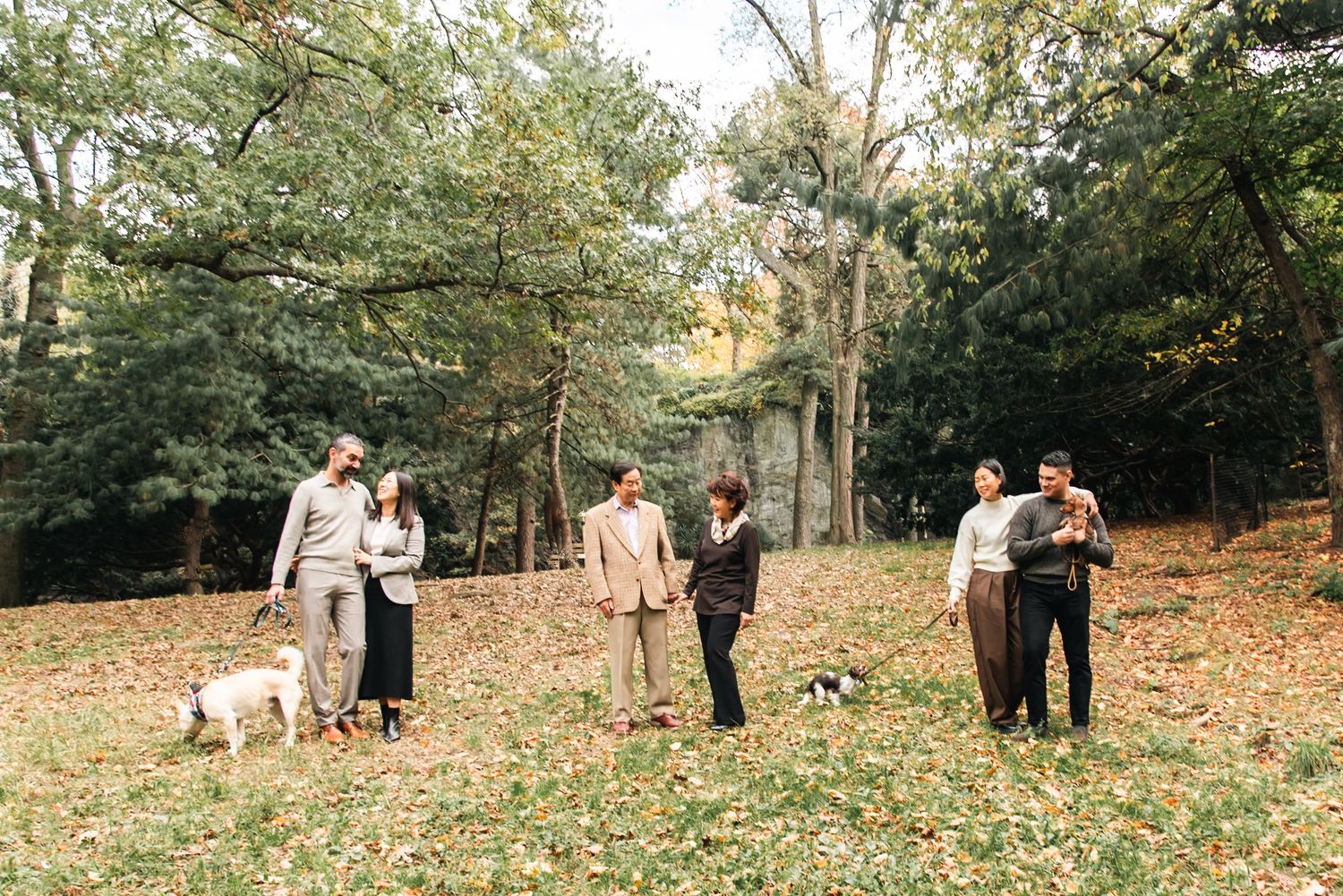 Family walking together through a wooded park with fallen autumn leaves.