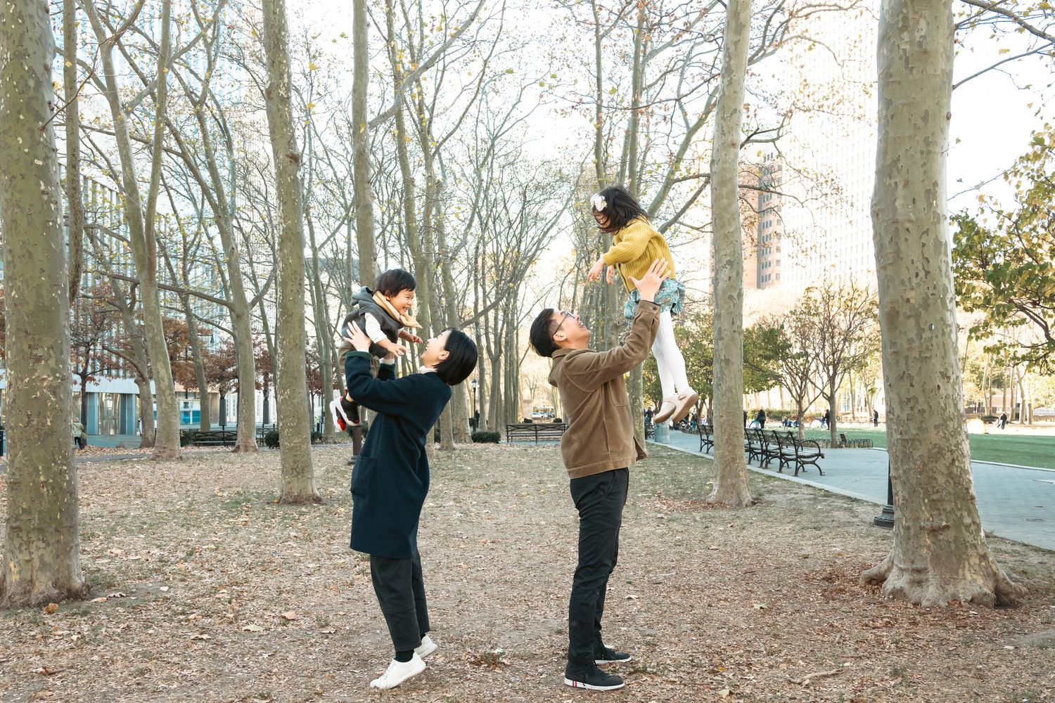 Playful family interaction among bare trees in a park during autumn.