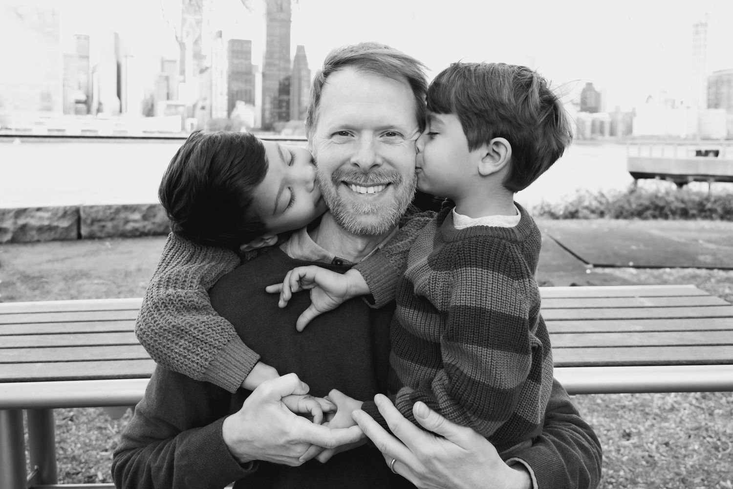 Tender family moments shared on a park bench with urban skyline in background.