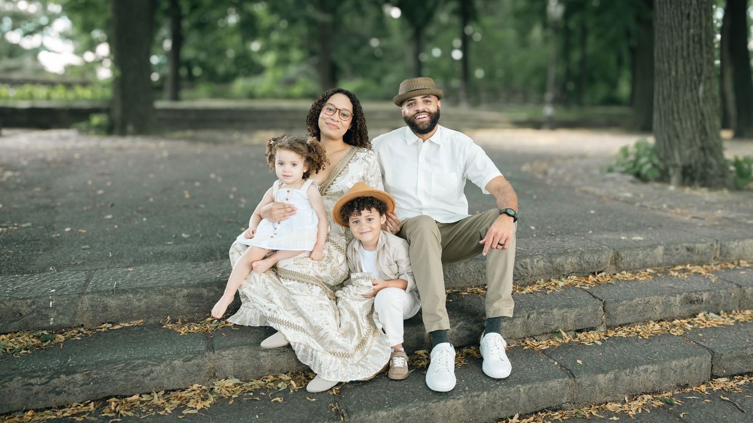 Happy family of four sitting on stone steps in a park, parents with young boy and girl on a sunny day.