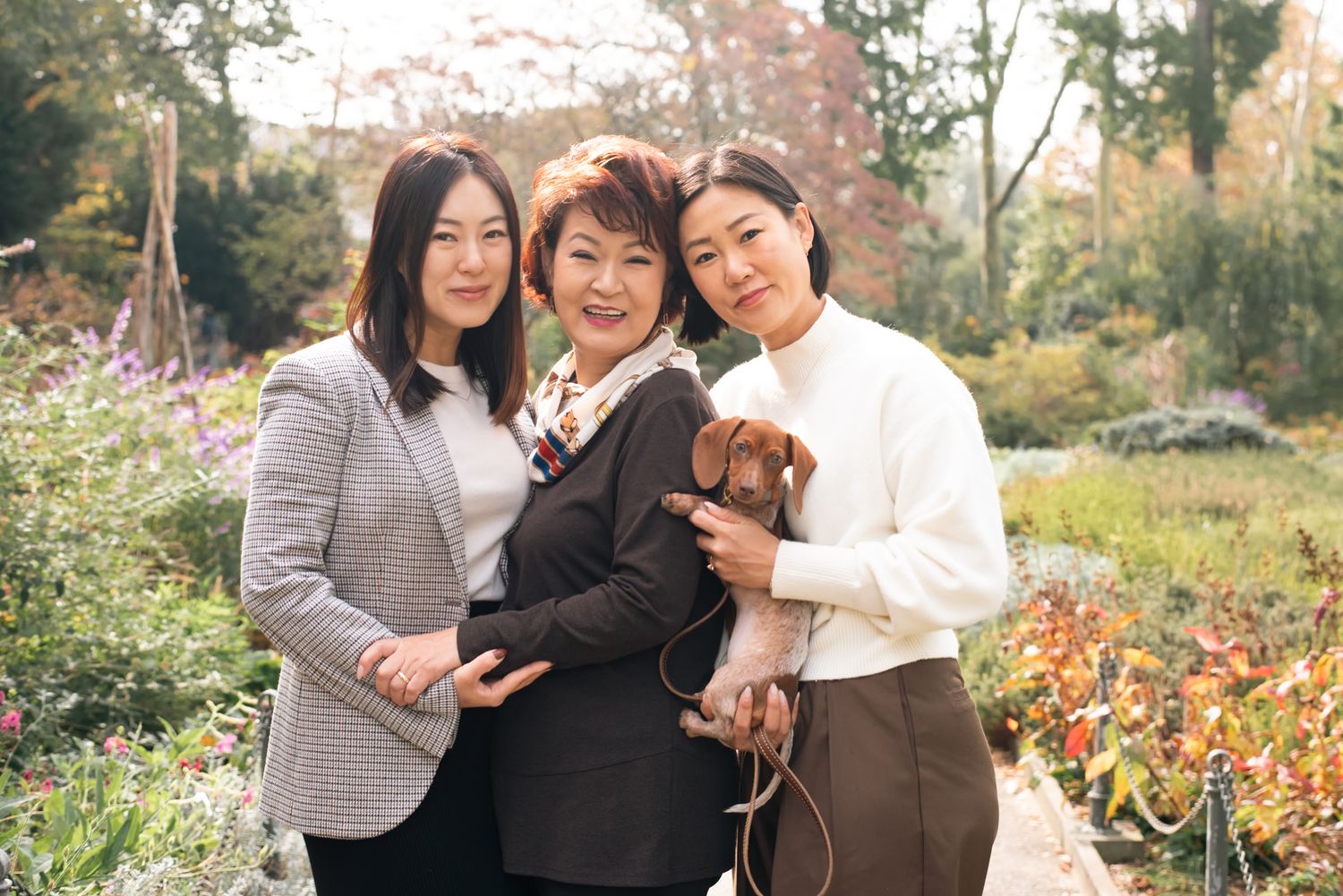 Three people sharing warm hugs and laughter in an autumn garden setting.