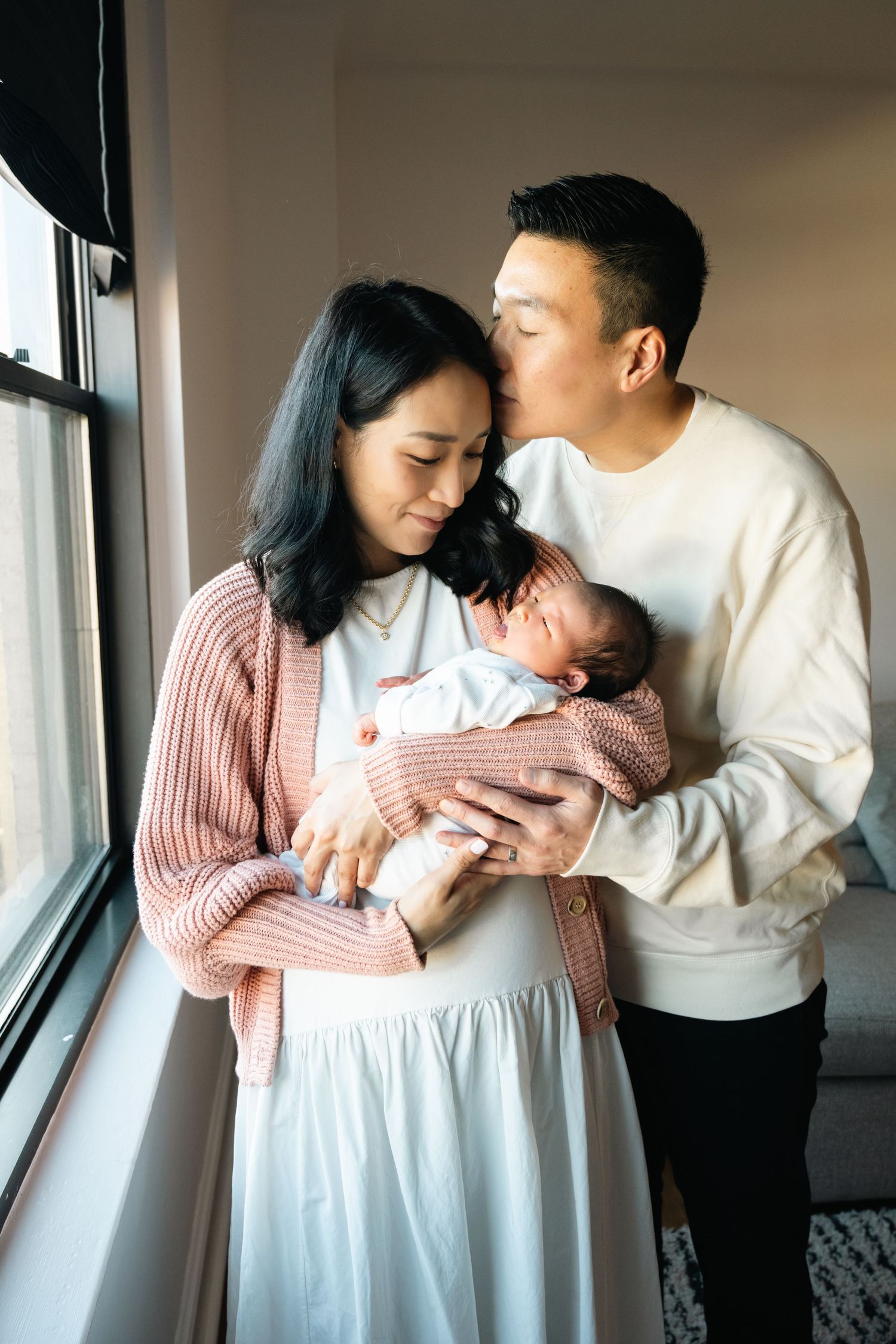 Family posing by window in natural light during indoor photography session.