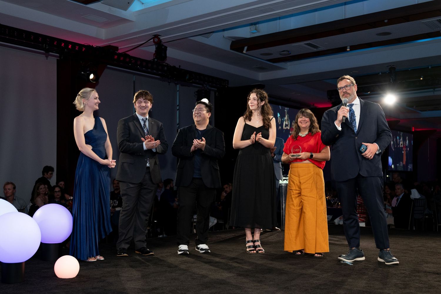 Six award recipients stand on stage together at the LUMEN IESNYC gala awards ceremony.