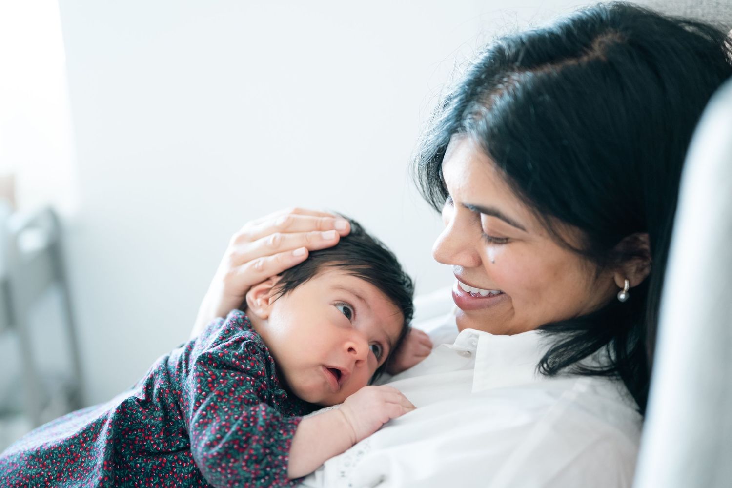 A smiling mother gently holds her newborn baby, cradling the infant close while tenderly touching its head.