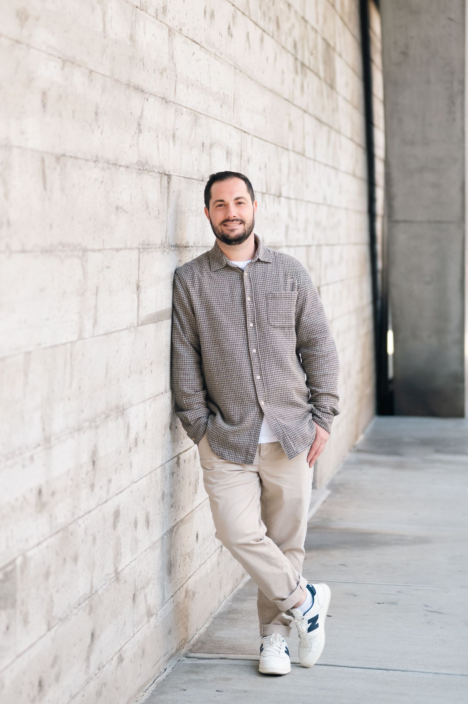 Casual portrait of man in gray shirt and khakis leaning against concrete wall.