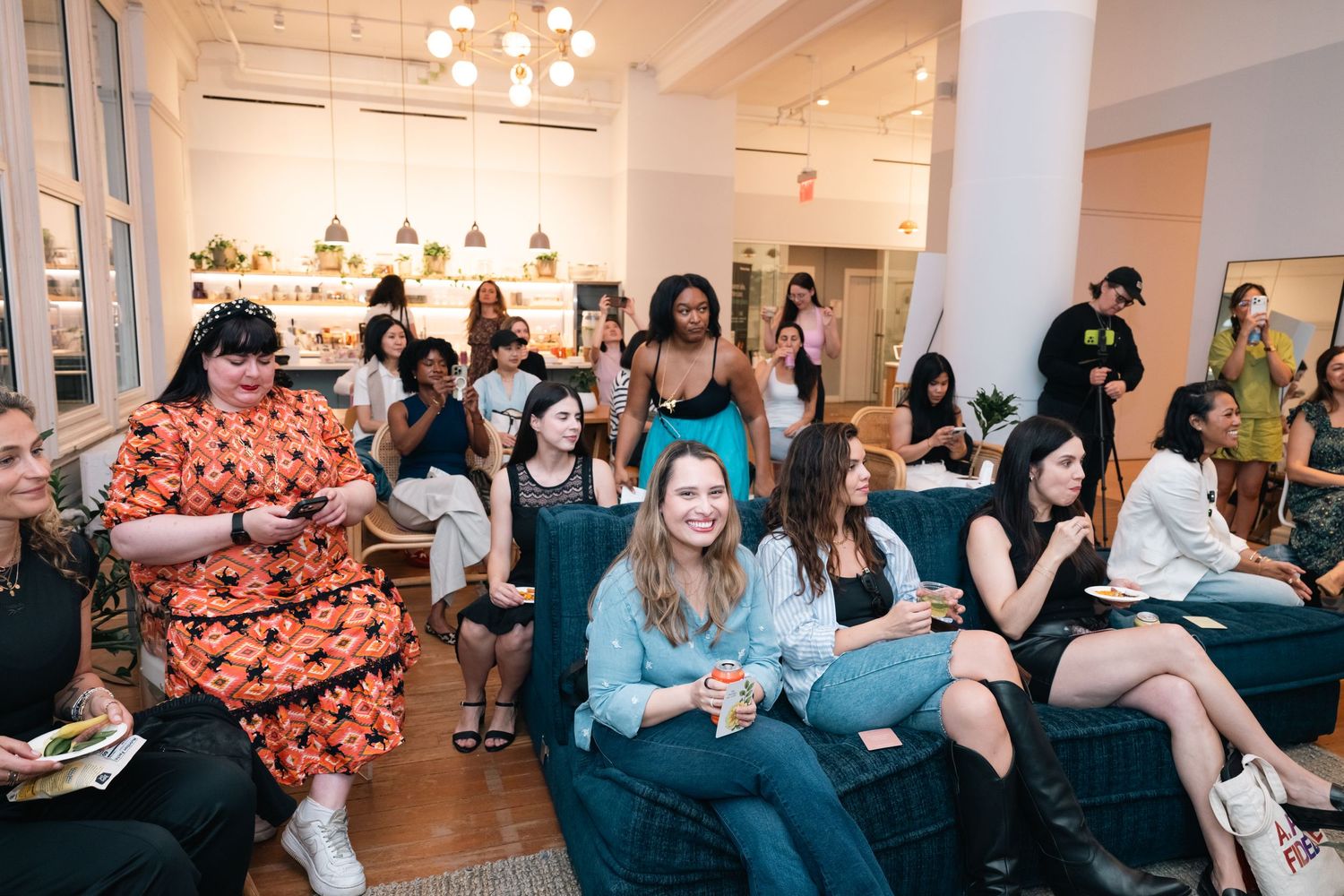Diverse group of women gathered at a stylish indoor event, seated and socializing in a modern, well-lit space.
