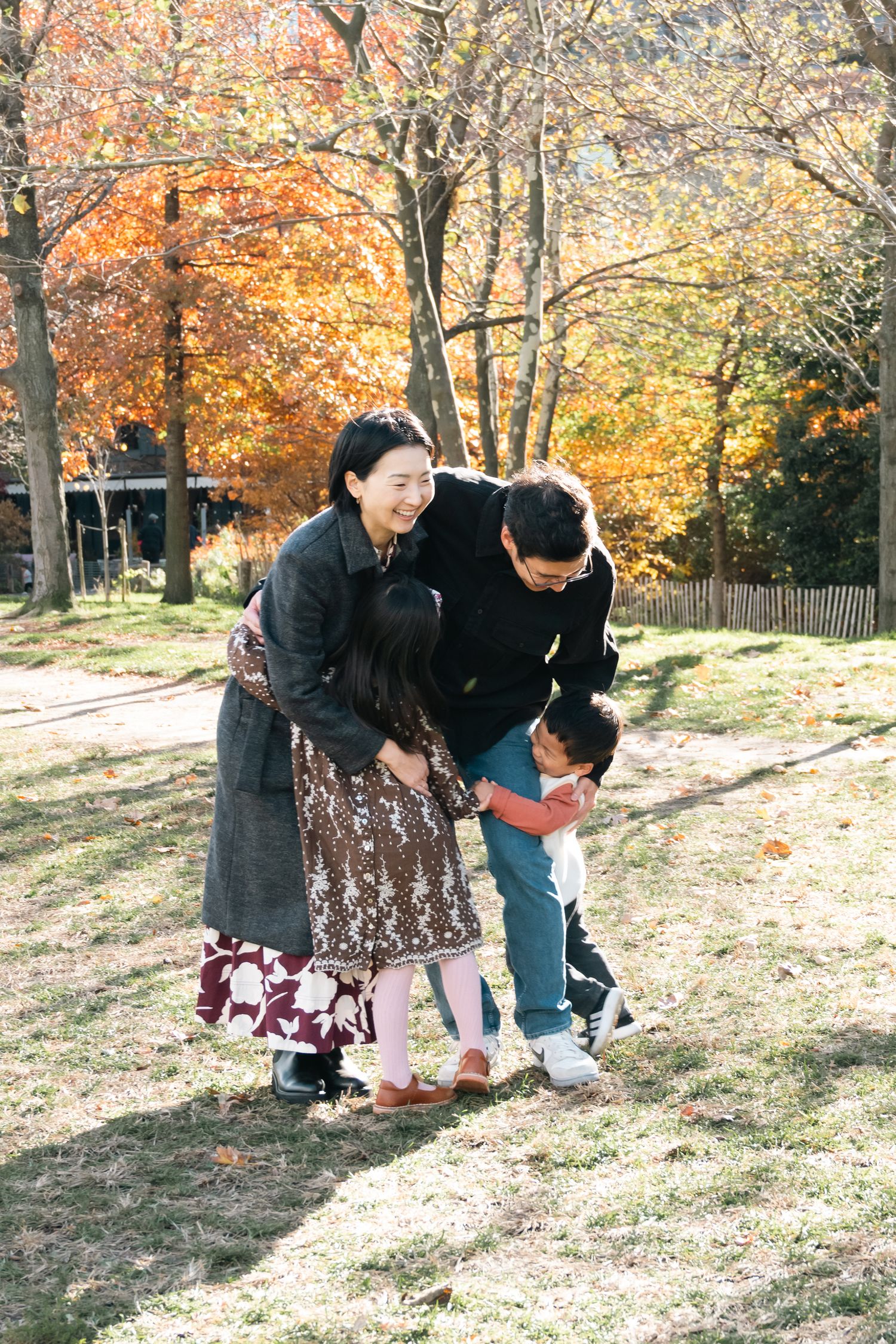 Two people in autumn clothing bend down to look at something on the ground surrounded by fall foliage in a park setting.