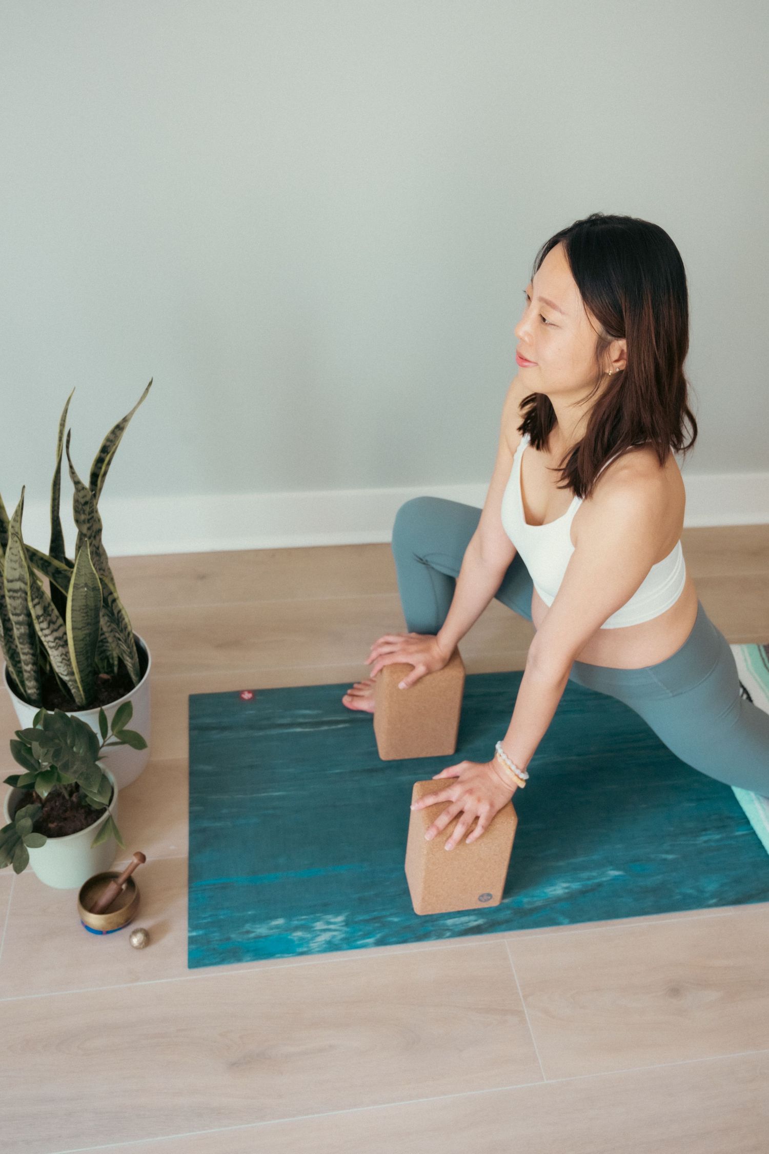 Demonstration of yoga stretching exercises using wooden blocks on a teal mat near potted plants.