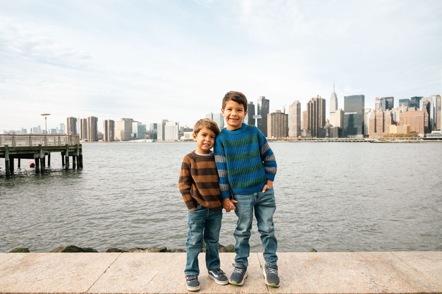 Family enjoying a scenic walk along a waterfront boardwalk with Manhattan skyline in the background.