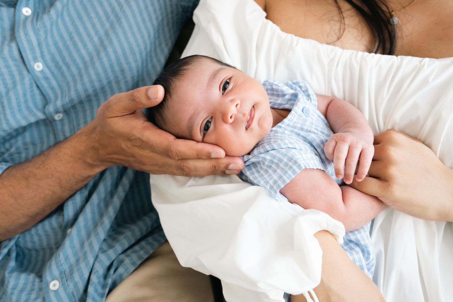 Close-up of newborn baby being cradled by parents' hands while wearing light blue outfit.