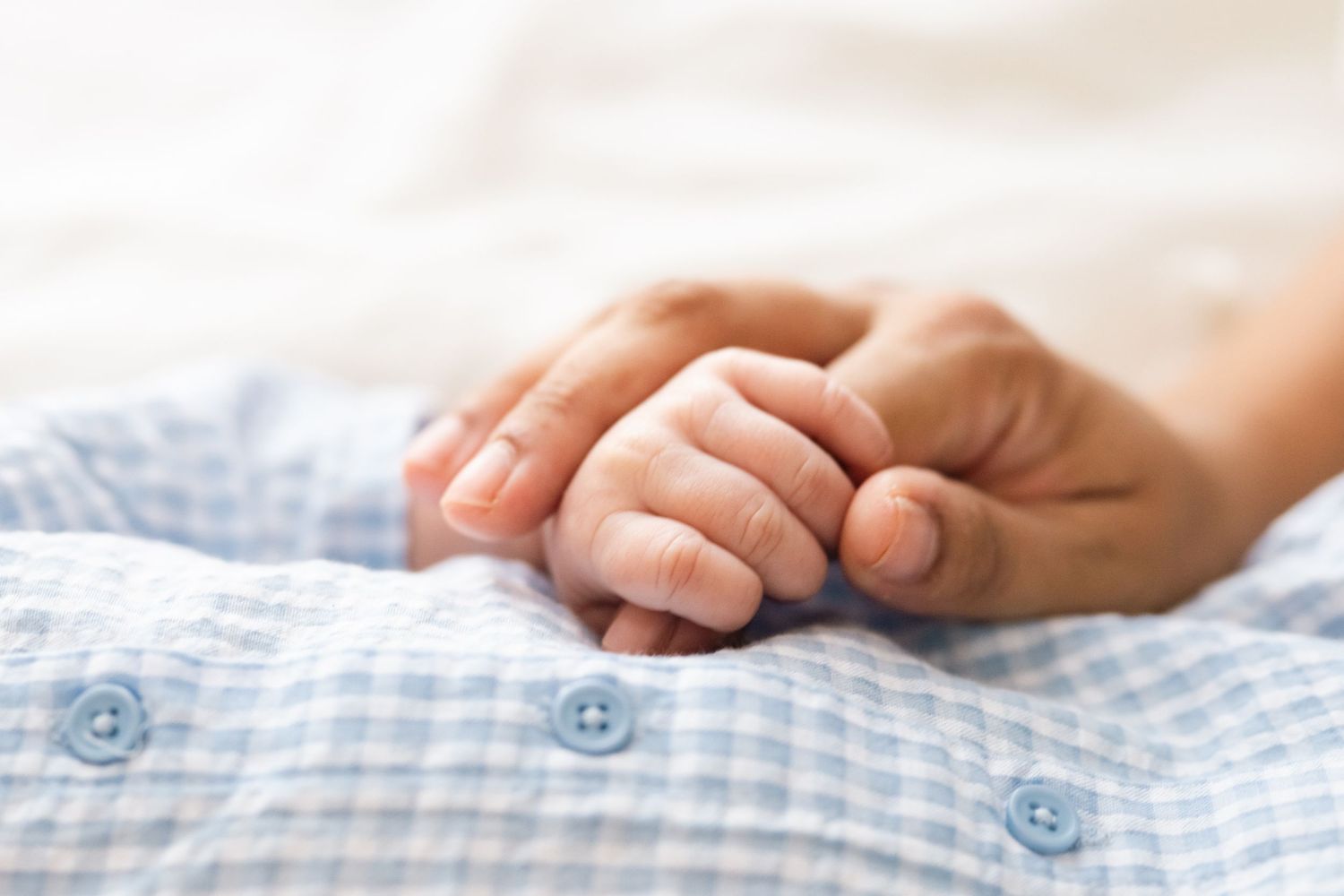 Close-up detail of hands resting on light blue gingham fabric.