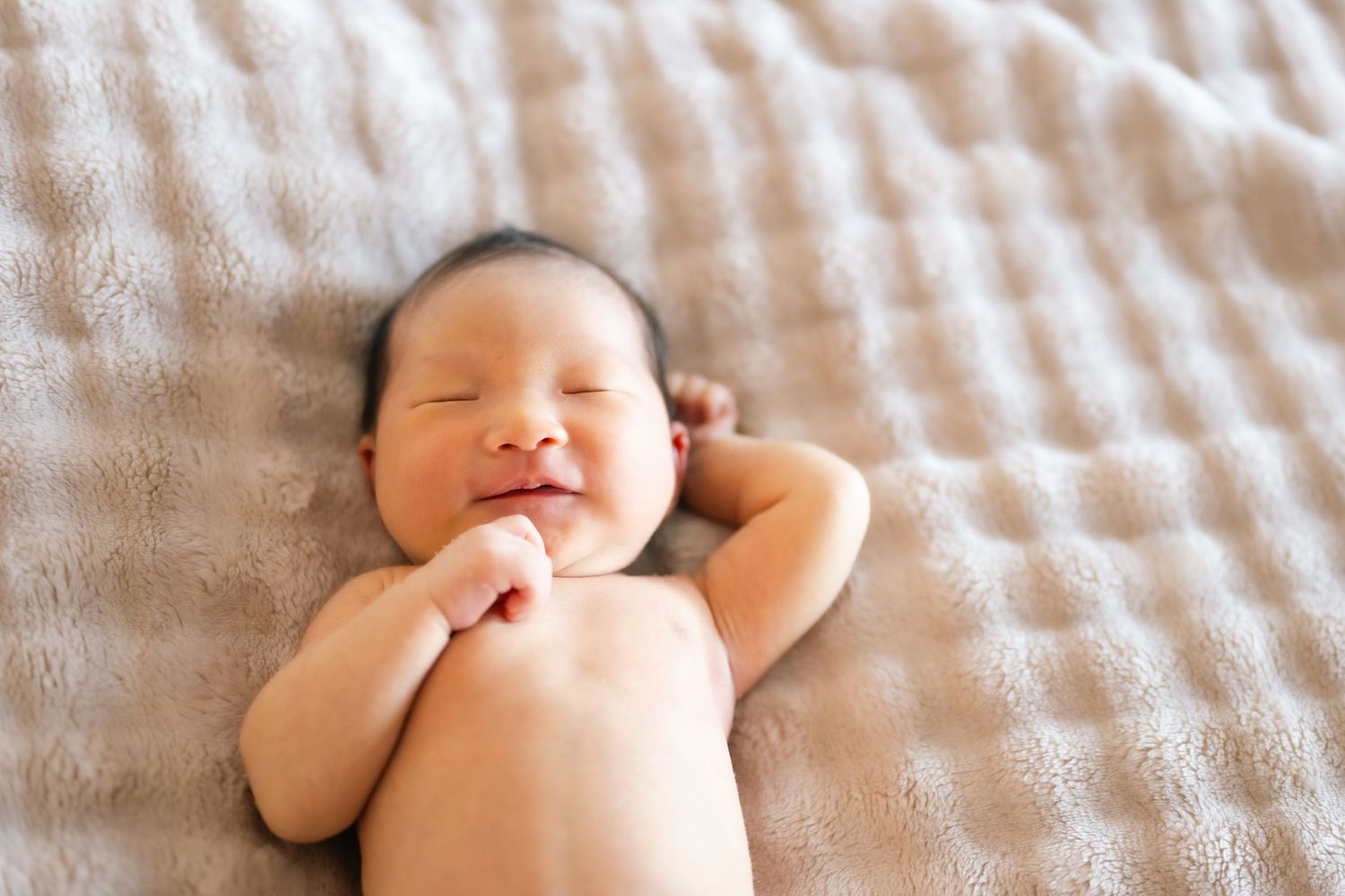 Peaceful sleeping newborn resting on textured white blanket.