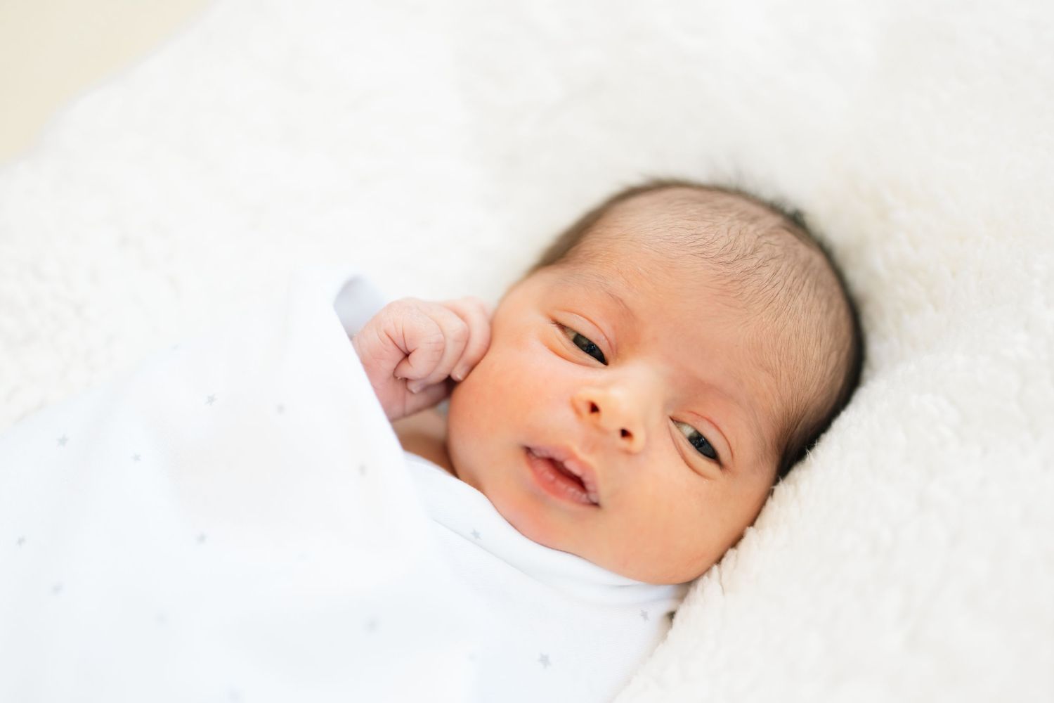 Series of gentle newborn portraits showing baby's peaceful expressions on white bedding.