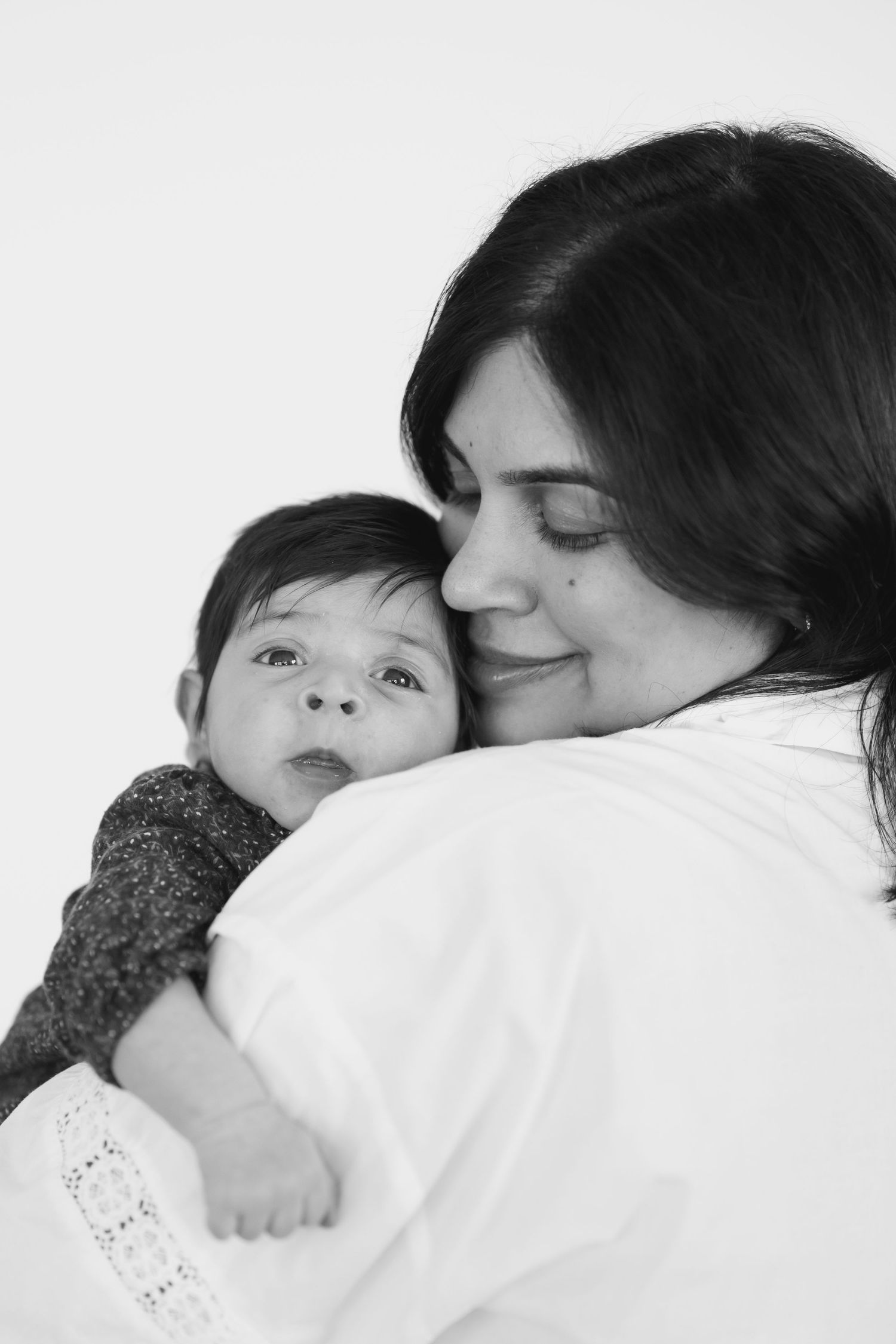 Black and white photo of a dark-haired woman tenderly holding and nuzzling a wide-eyed baby in her arms.