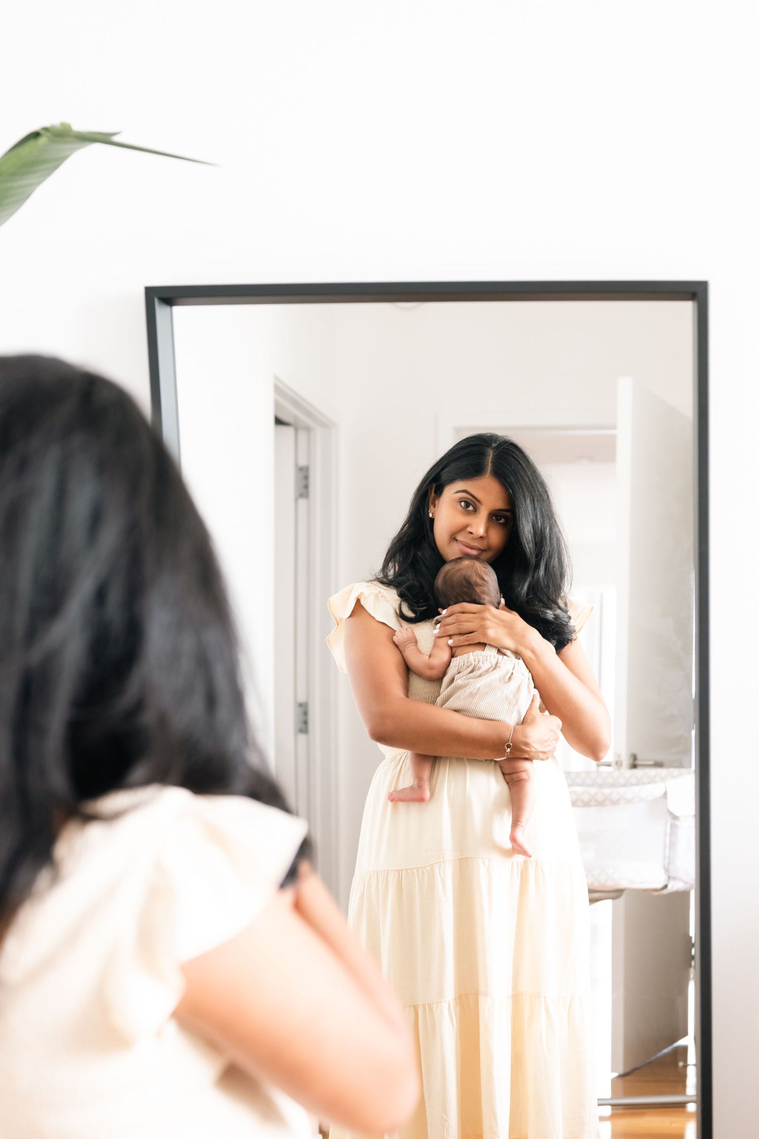 Woman in white dress looking at her reflection in a full-length mirror.