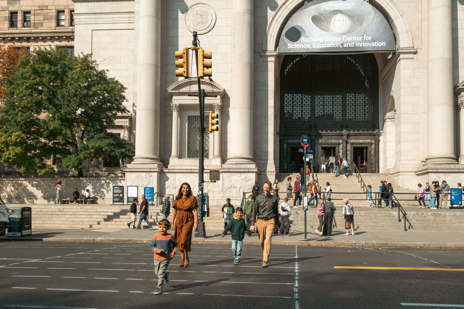 Pedestrians crossing street in front of grand architectural building with columns.