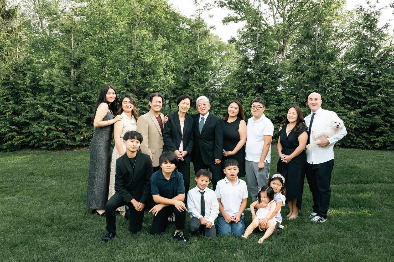 Group photo of people gathered outdoors on a green lawn with hedges in the background.