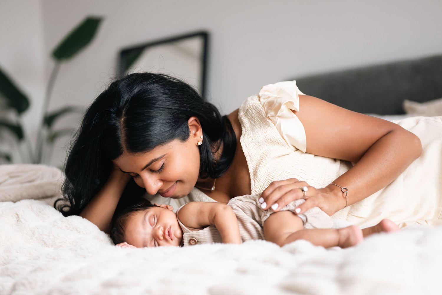 Tender moment between parent and baby lying together on white bedding.
