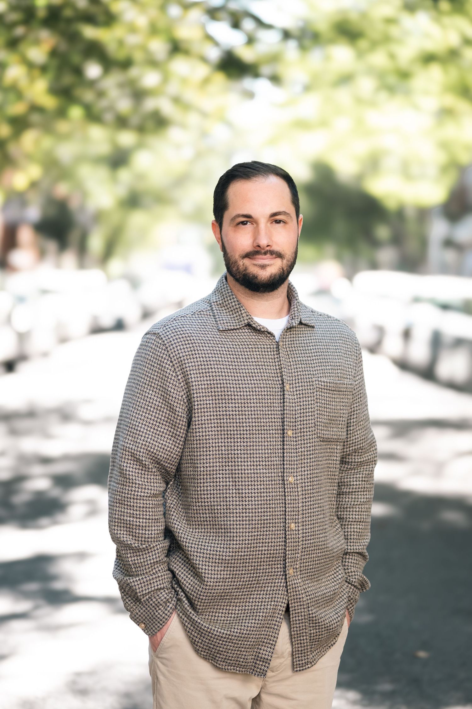 Portrait of man in houndstooth jacket on tree-lined street.