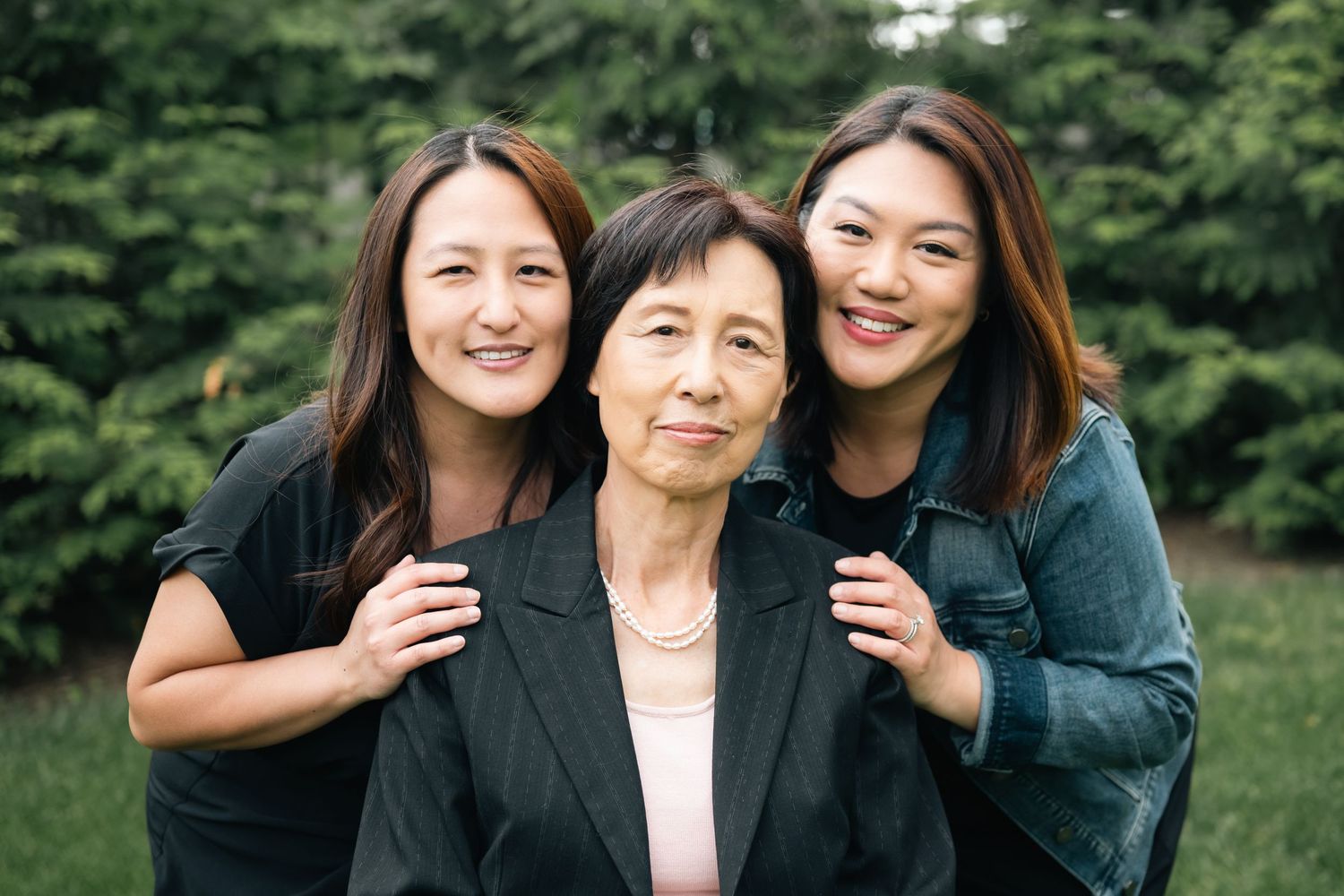 A family photo session outdoors with multiple generations wearing formal attire against a green backdrop.