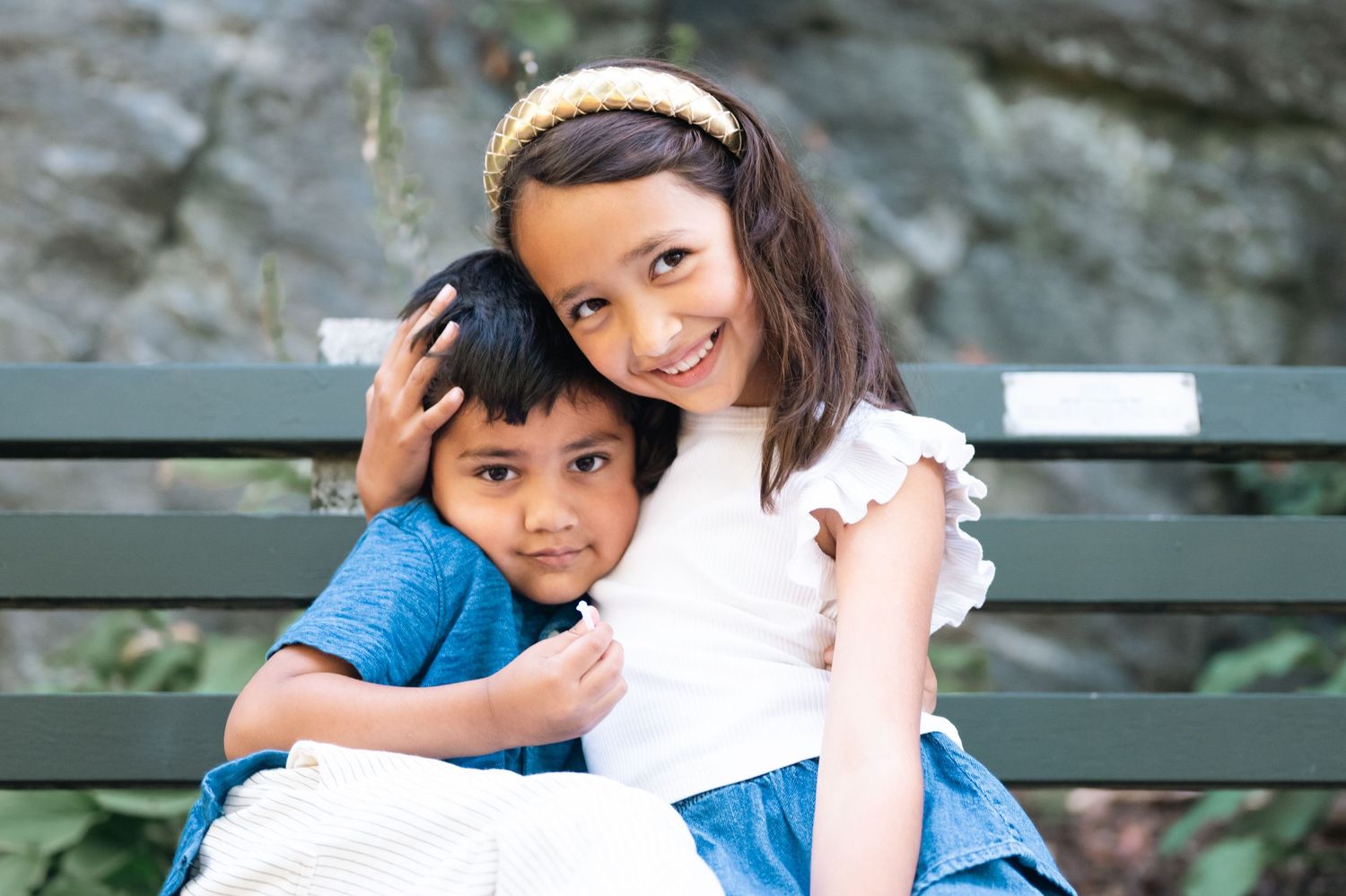 Two children sitting close together on a green park bench sharing a tender moment.