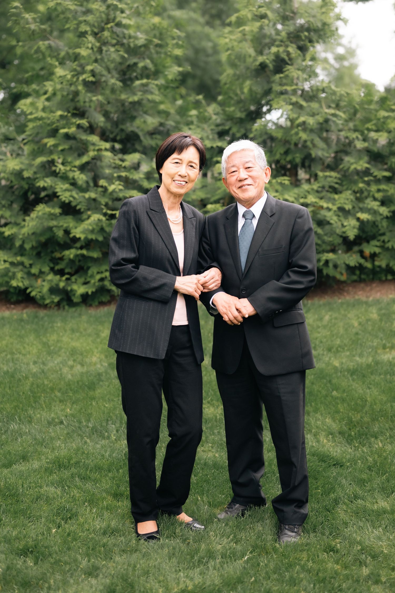 Two people in formal business attire share a candid moment while standing on grass.