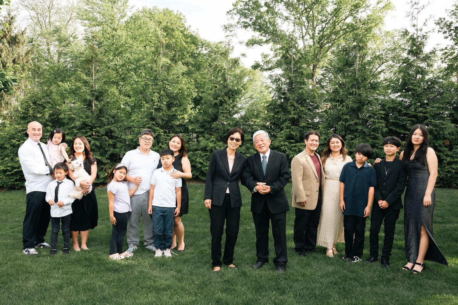 Extended family portrait series taken outdoors with green trees in background.