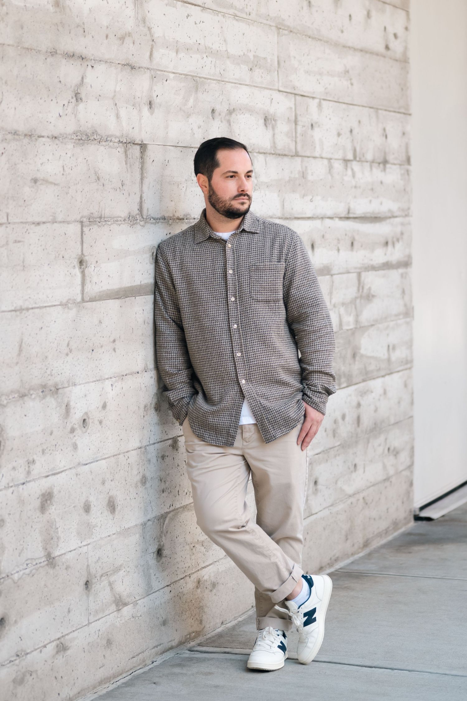 Man in casual attire posing against textured concrete wall.