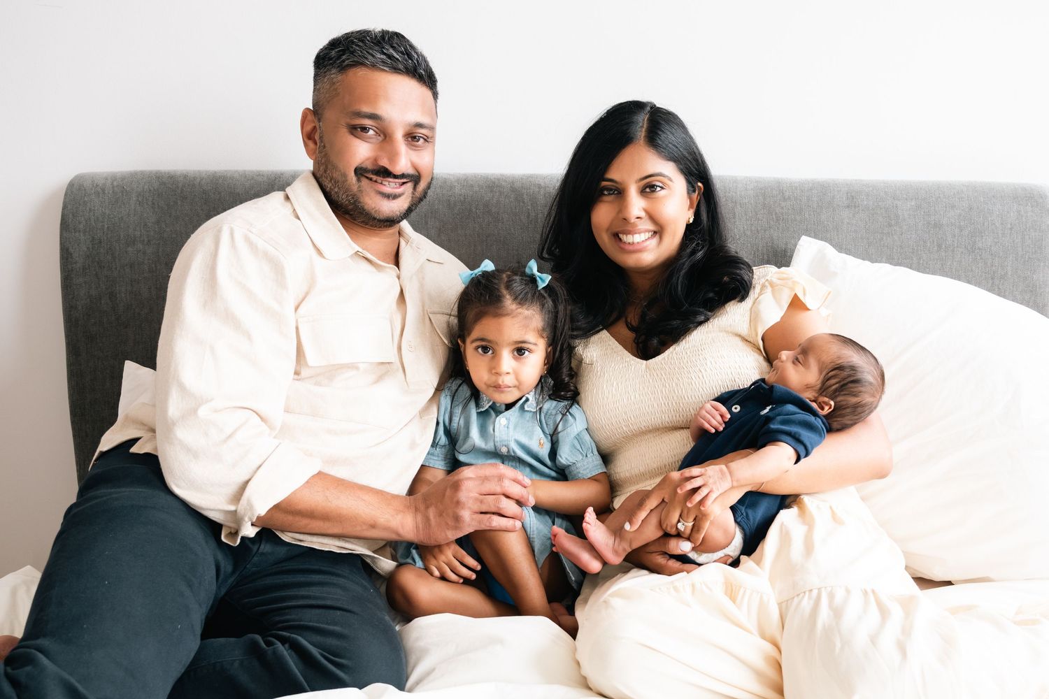 Family relaxing together on a light gray couch in casual white and navy outfits.
