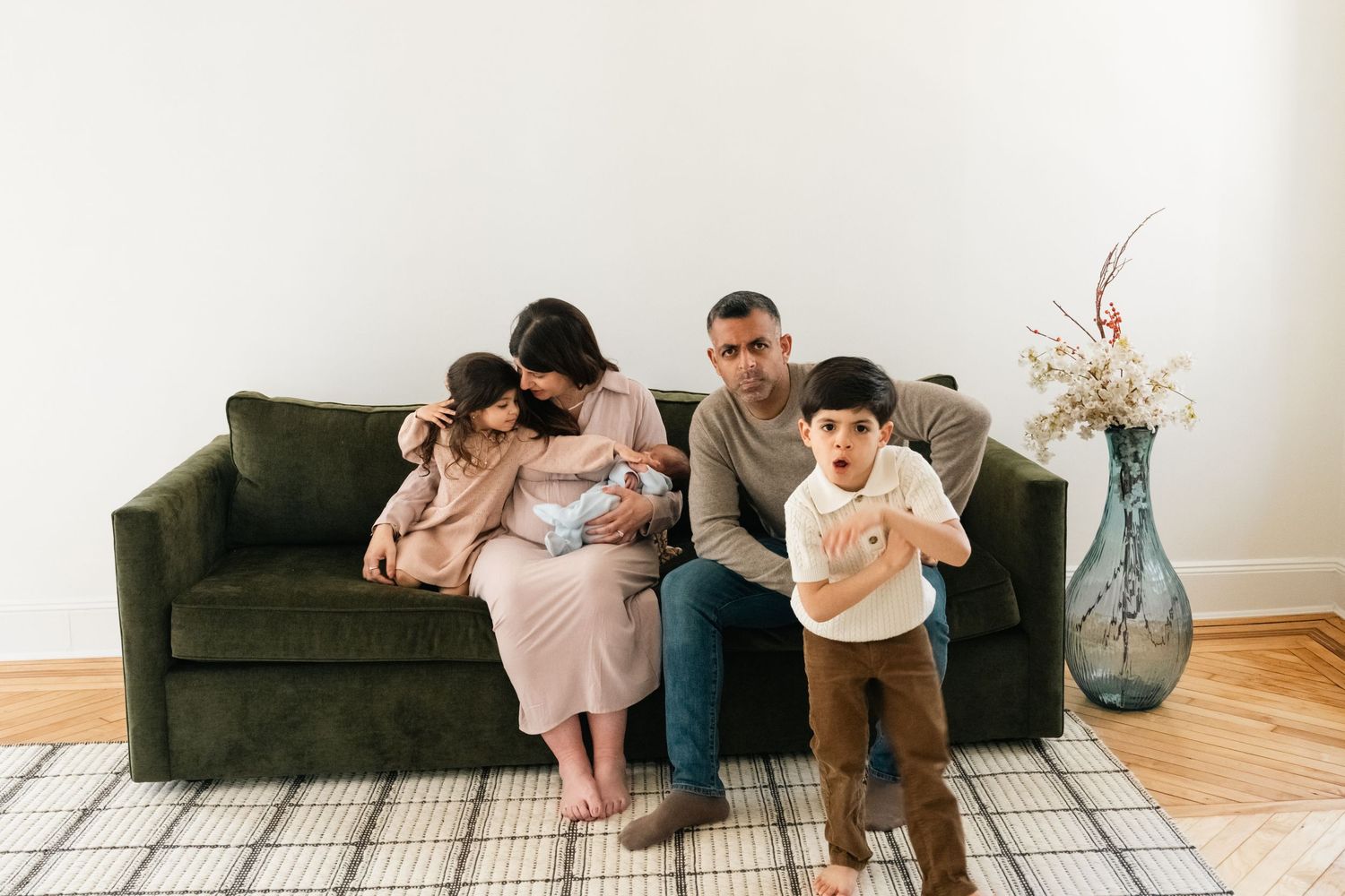 Modern family lifestyle session showing natural interactions on grey couch in bright white room.