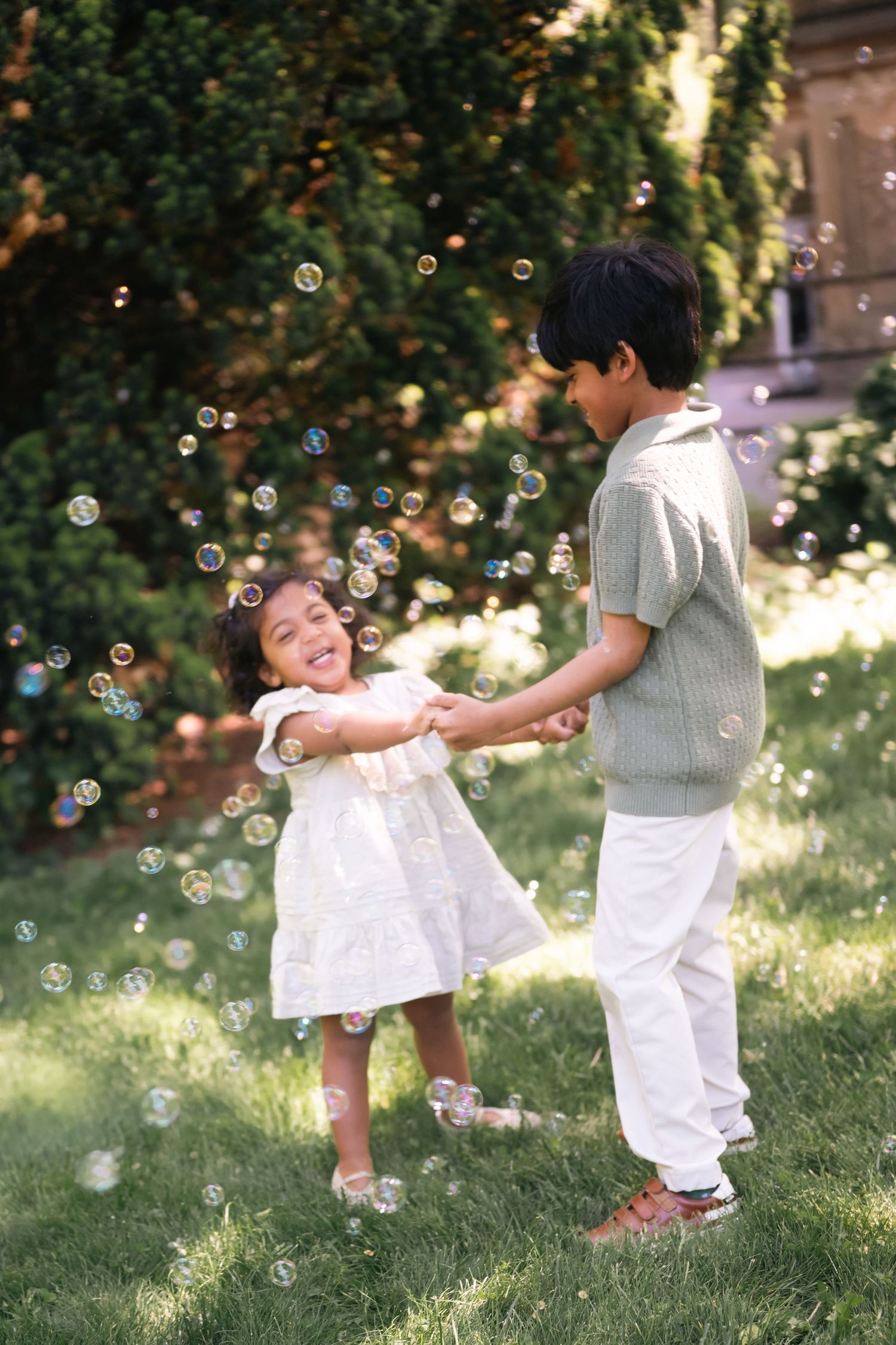 Two children playing joyfully outdoors surrounded by floating soap bubbles on a sunny green lawn.