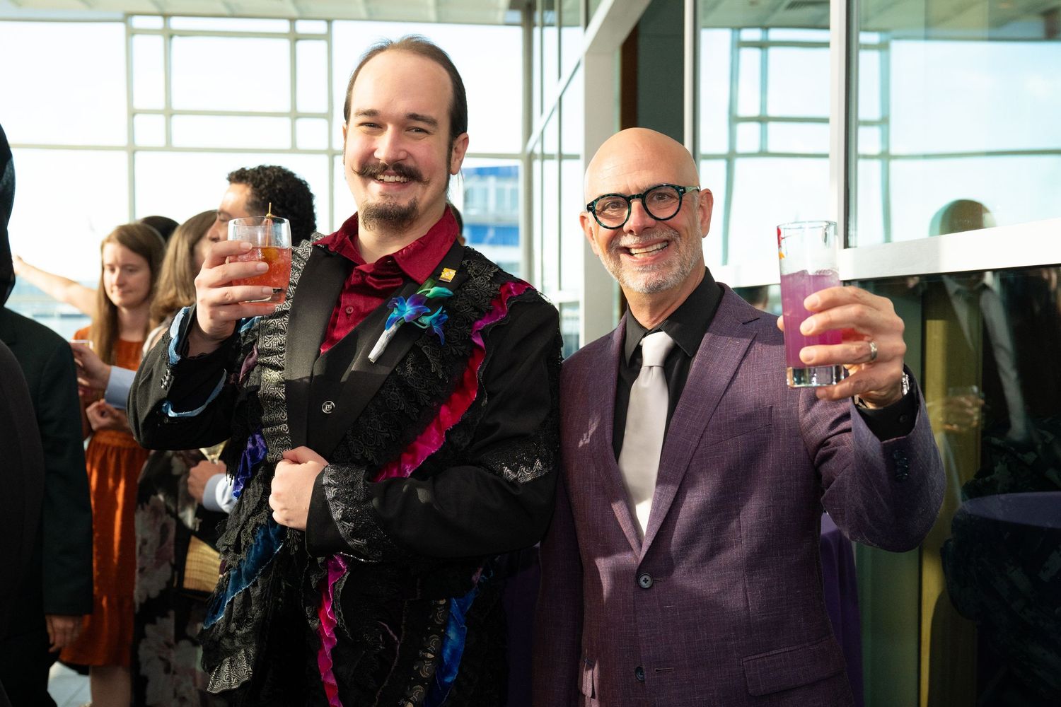 Two smiling men in festive attire toasting drinks at an elegant party event.