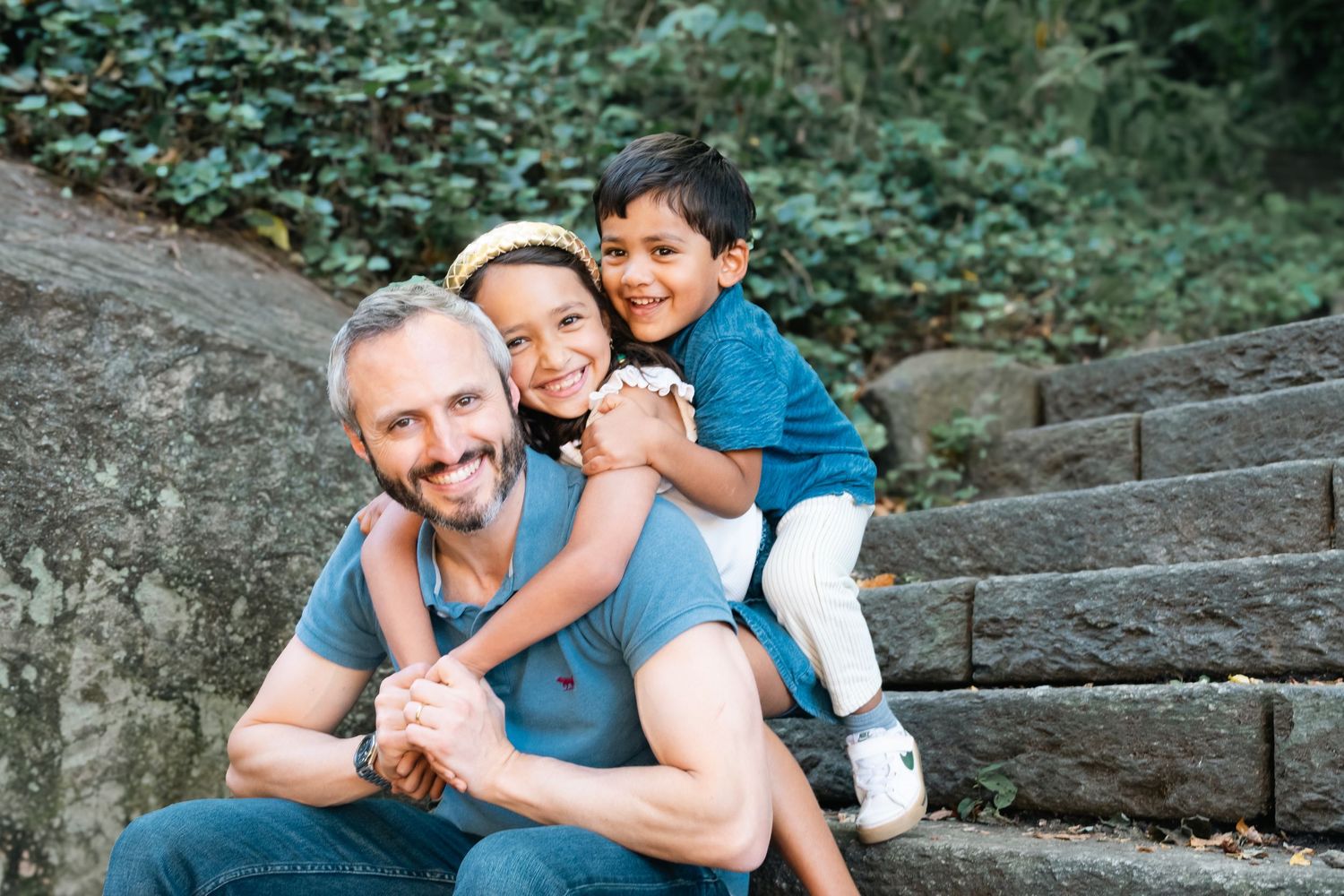 A family sits together on stone steps surrounded by lush greenery during an outdoor photo session.
