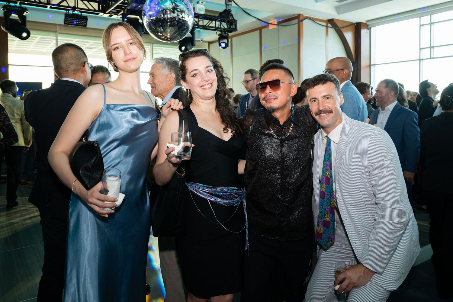 Four friends pose together smiling at an upscale indoor evening social event or gala.
