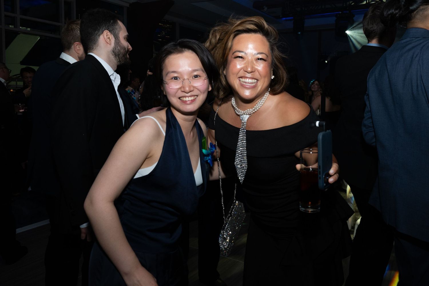 Two women smiling and posing together at an upscale evening social event.