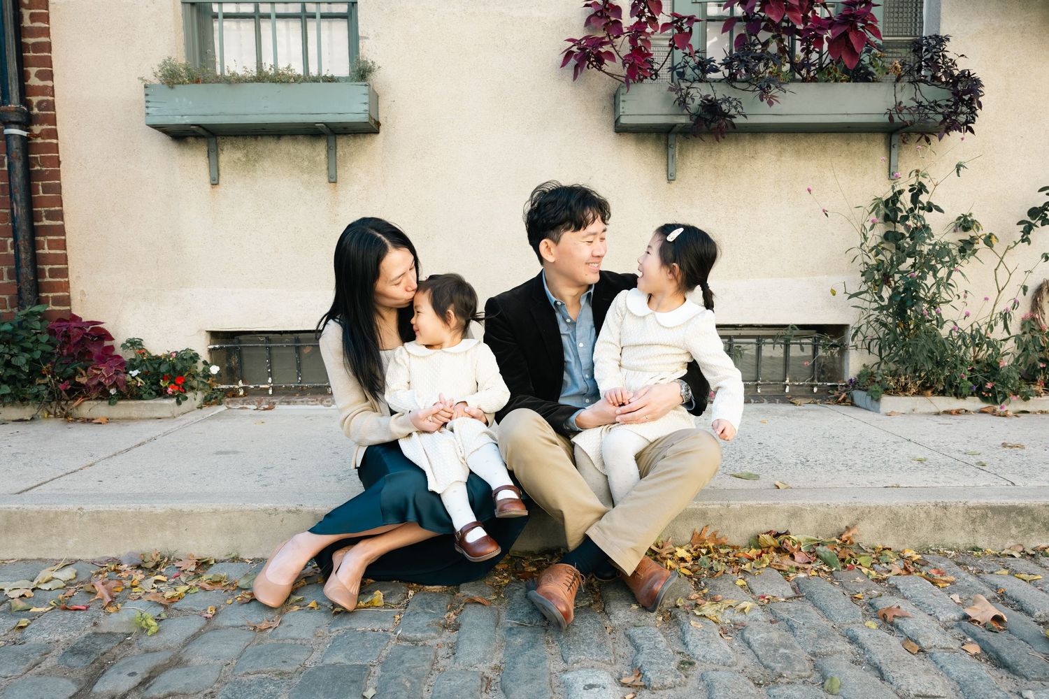 Family sitting together on stone steps outside a building with flower boxes.