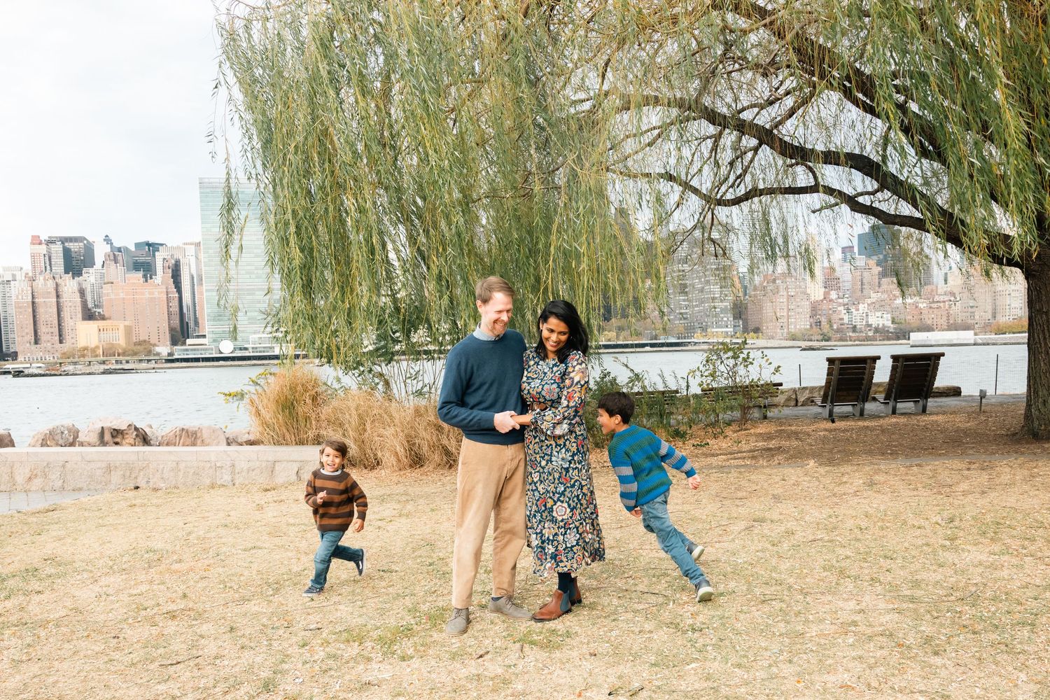 Family playing together in a grassy park area near willow trees.