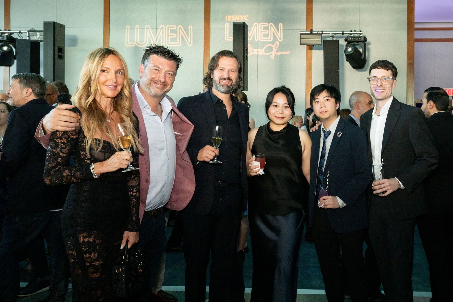 Six formally dressed guests posing together at a sophisticated evening reception with elegant venue lighting.