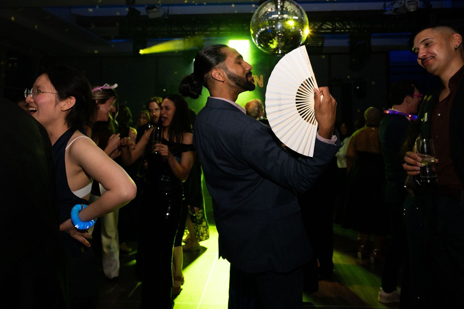 Guests dance and celebrate under green lights and a disco ball at a lively evening party.