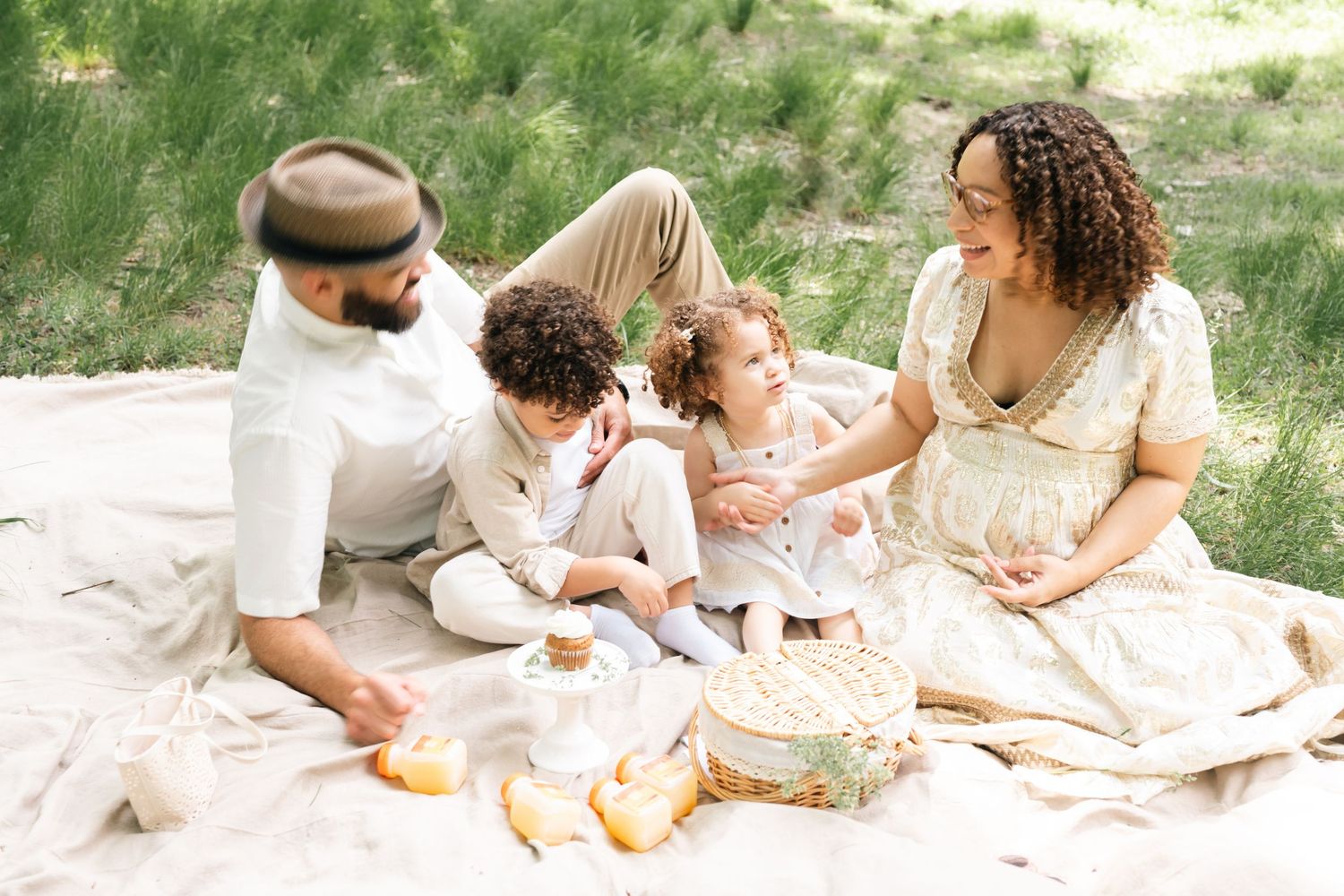 A joyful multiracial family enjoys a sunny outdoor picnic on a blanket surrounded by green grass.