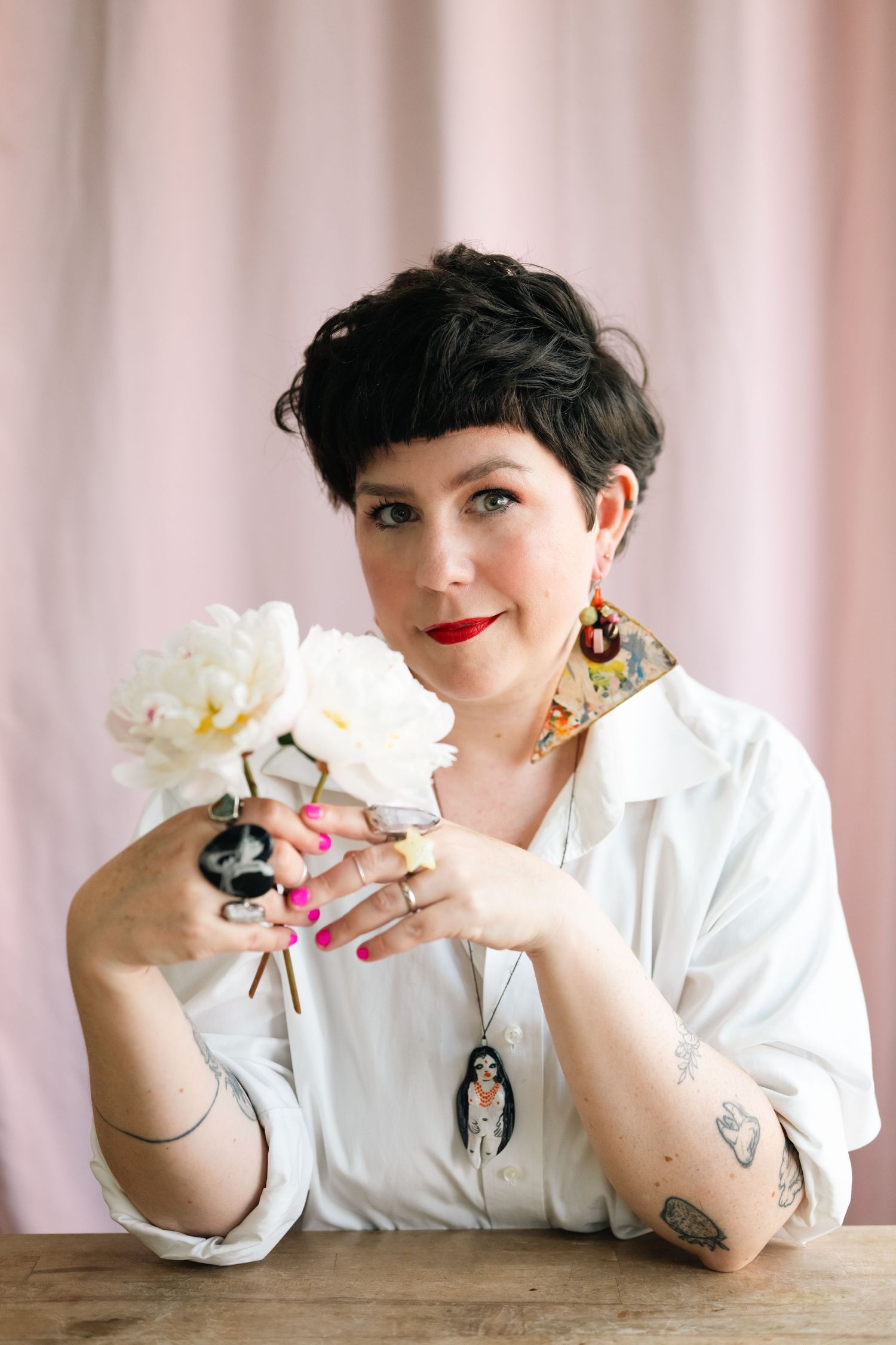 Person in white shirt holding white peonies against pink backdrop.